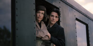Eine Frau und ein Mann schauen aus der Tür eines Zuges, nahe zuammengerückt