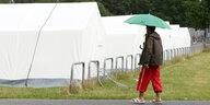 ein Mann mit Regenschirm geht an ei ner Reihe weißer Zelte vorbei