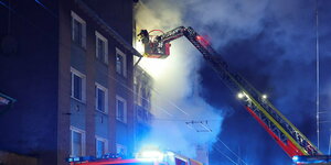 Von einer Drehleiter aus bekämpft ein Feuerwehrmann den Brand in einem Mehrfamilienhaus in Solingen