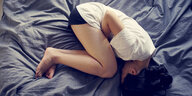 eine Frau liegt gekrümmt auf einem Bett