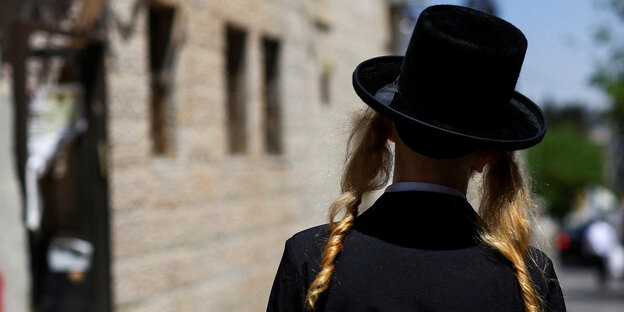 Ein ultraorthodoxer Jude mit blonden Schläfenlocken und Hut geht durch Mea Sharim in Jerusalem, er sit von hinten zu sehen