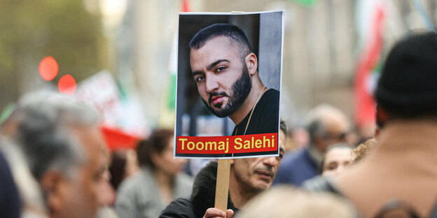 Ein Demonstrierender hält ein Schild mit dem Portät vom Papper Toomaj Salehi in die Höhe.