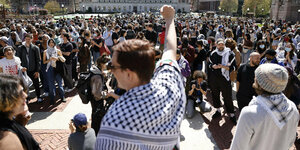 Eine Person mit Palestinensertuch steht vor einer Menschenmenge und reckt die Faust